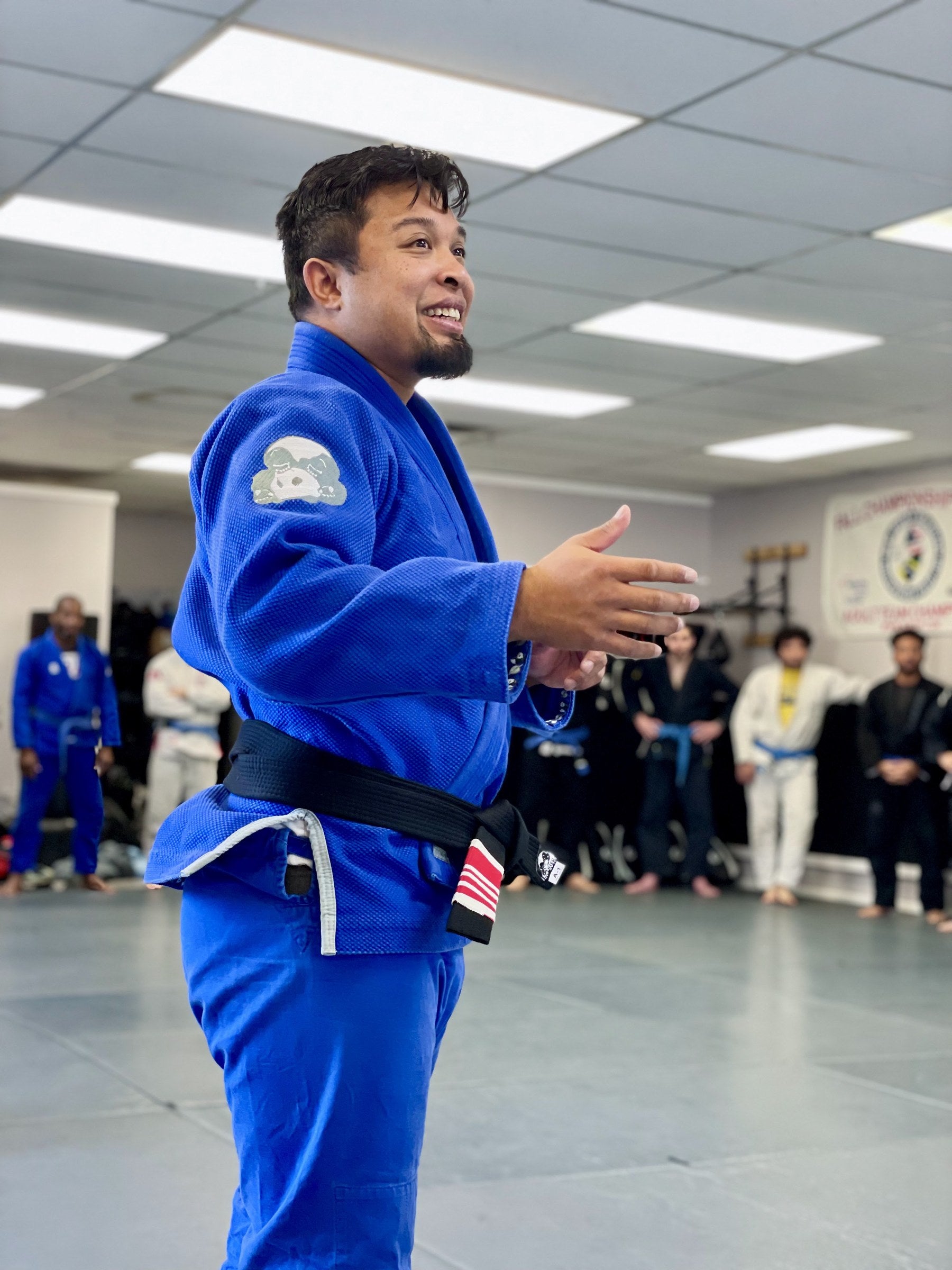 An instructor in a blue Panda gi teaching a class lined up along the wall